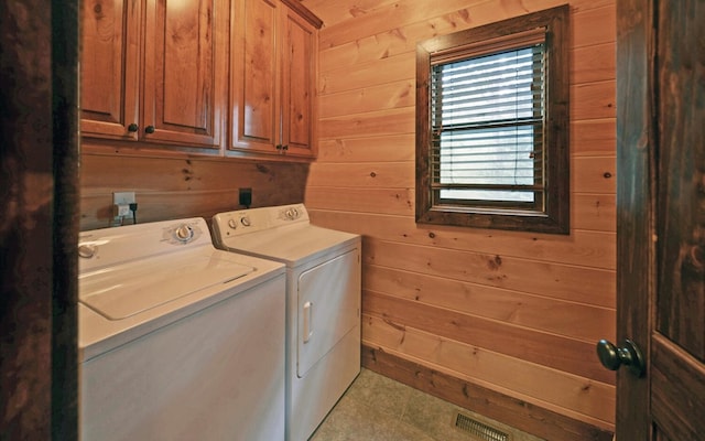 washroom featuring washing machine and clothes dryer, wood walls, cabinet space, and tile patterned floors