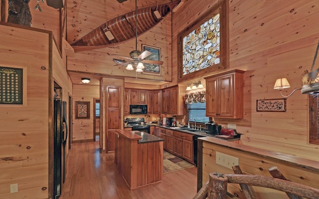 kitchen with black appliances, wood walls, high vaulted ceiling, a sink, and light wood-style floors