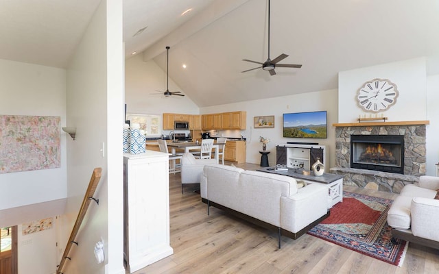 living room with ceiling fan, high vaulted ceiling, beamed ceiling, light hardwood / wood-style floors, and a stone fireplace