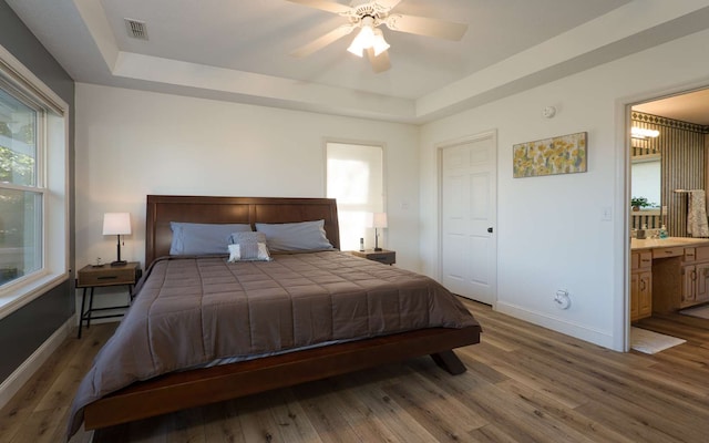 bedroom with hardwood / wood-style floors, ensuite bath, ceiling fan, and a tray ceiling