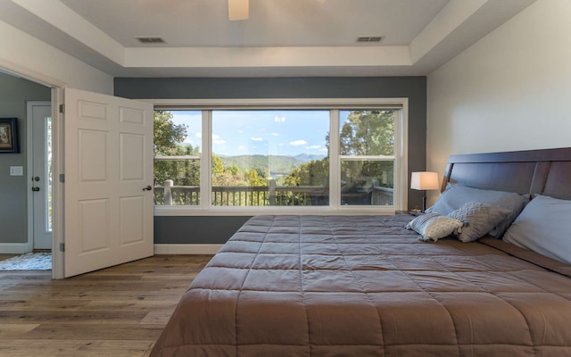 bedroom featuring hardwood / wood-style flooring, a mountain view, ceiling fan, and a raised ceiling