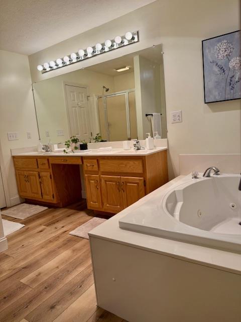 bathroom with plus walk in shower, wood-type flooring, vanity, and a textured ceiling