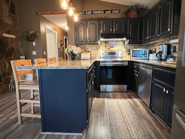 kitchen featuring a kitchen bar, backsplash, stainless steel appliances, vaulted ceiling, and dark hardwood / wood-style floors