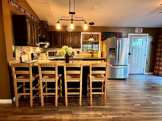 kitchen featuring dark hardwood / wood-style flooring, a kitchen bar, sink, dark brown cabinetry, and stainless steel appliances