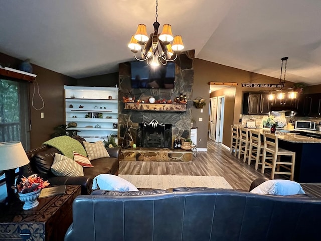 living room featuring vaulted ceiling, a stone fireplace, light wood-type flooring, and an inviting chandelier