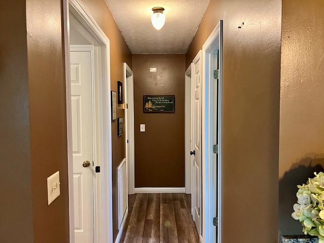 corridor with a textured ceiling and dark hardwood / wood-style floors