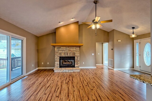 unfurnished living room with a stone fireplace, plenty of natural light, lofted ceiling, and light wood-type flooring