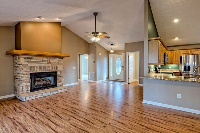 interior space with a stone fireplace, ceiling fan, light wood-type flooring, light stone countertops, and stainless steel appliances