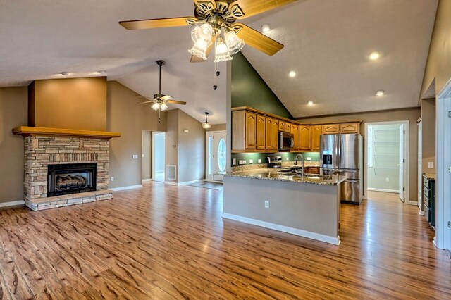 kitchen featuring a stone fireplace, kitchen peninsula, stone countertops, appliances with stainless steel finishes, and light wood-type flooring