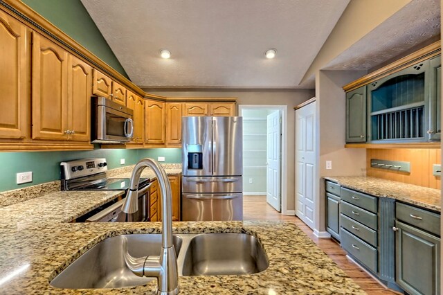 kitchen featuring light stone counters, sink, stainless steel appliances, and lofted ceiling