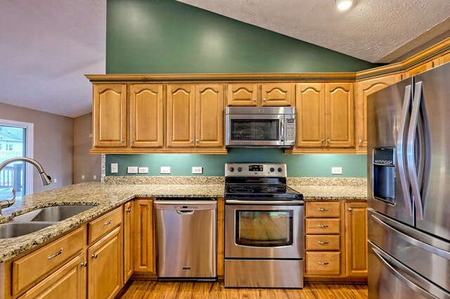 kitchen featuring lofted ceiling, sink, light stone countertops, light wood-type flooring, and appliances with stainless steel finishes