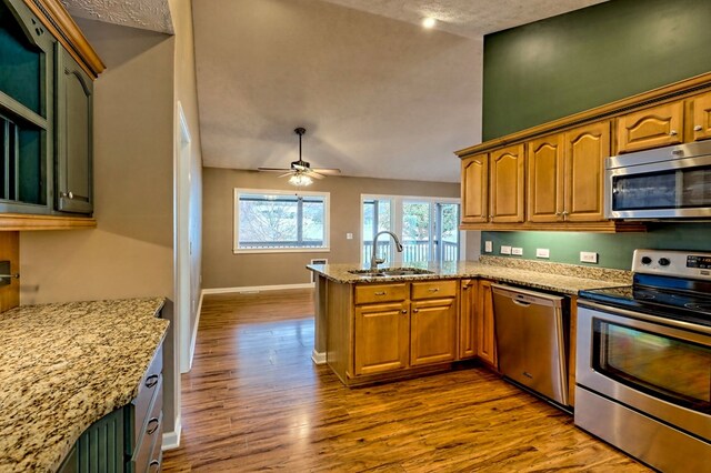 kitchen featuring kitchen peninsula, light wood-type flooring, stainless steel appliances, ceiling fan, and sink