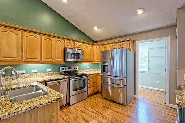 kitchen featuring sink, stainless steel appliances, light stone counters, light hardwood / wood-style floors, and lofted ceiling