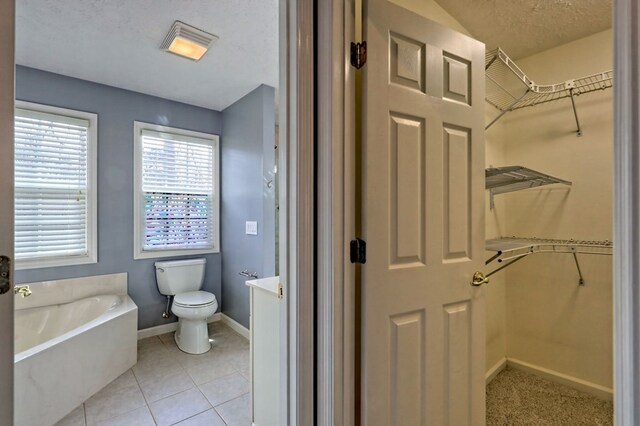 bathroom with tile patterned floors, a tub, a textured ceiling, and toilet