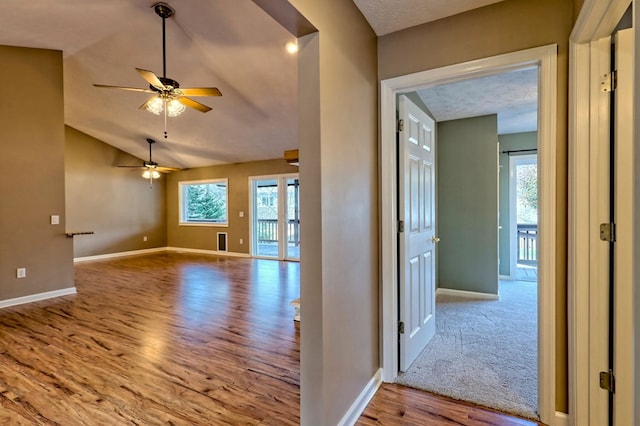 corridor with a textured ceiling, light hardwood / wood-style flooring, and vaulted ceiling