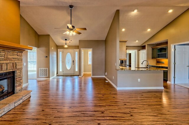 unfurnished living room with dark hardwood / wood-style flooring, ceiling fan, sink, high vaulted ceiling, and a fireplace