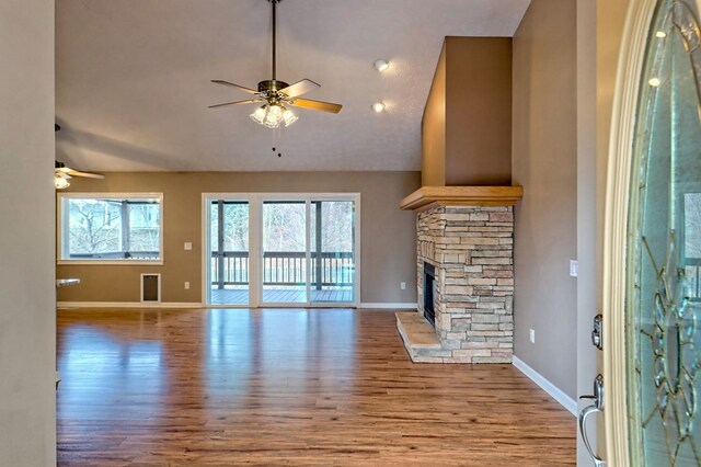 unfurnished living room featuring ceiling fan, a stone fireplace, and light wood-type flooring