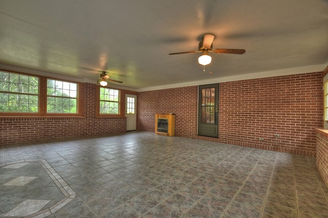 unfurnished living room featuring ceiling fan and brick wall