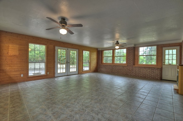 tiled empty room with ceiling fan, french doors, and brick wall