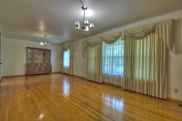 empty room featuring wood-type flooring and a notable chandelier