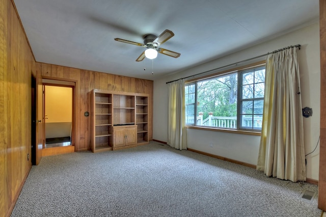 unfurnished bedroom featuring wood walls, ceiling fan, and light carpet