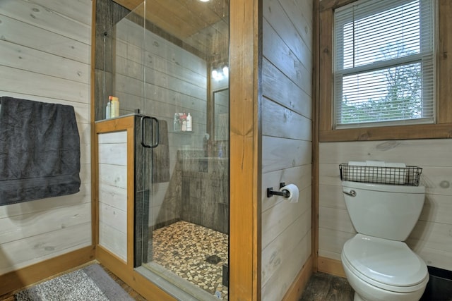 bathroom featuring wood walls, plenty of natural light, a shower with shower door, and toilet