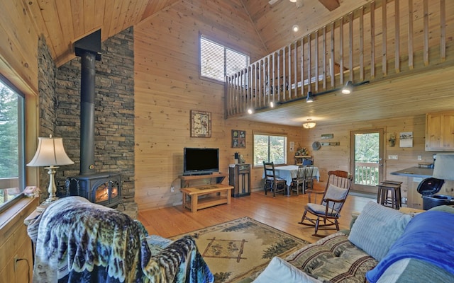 living room with wood walls, a wood stove, wood-type flooring, and high vaulted ceiling