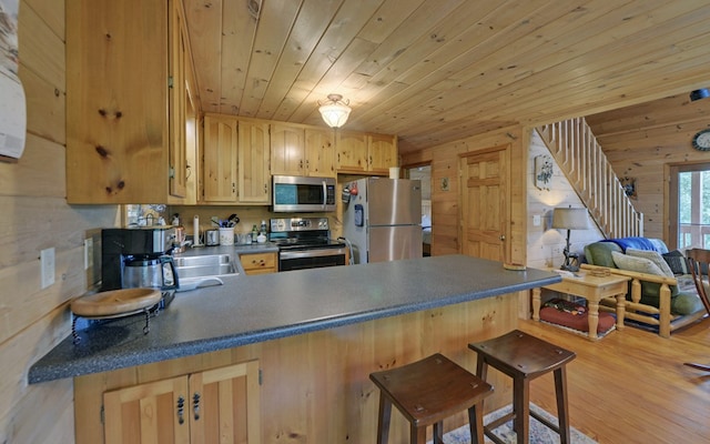 kitchen featuring wooden walls, stainless steel appliances, a breakfast bar, kitchen peninsula, and light wood-type flooring