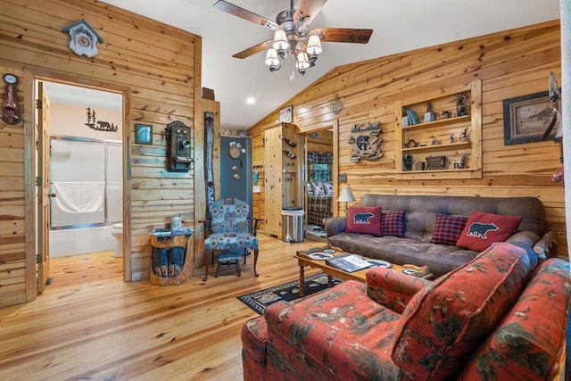 living room featuring a ceiling fan, vaulted ceiling, wooden walls, and wood finished floors