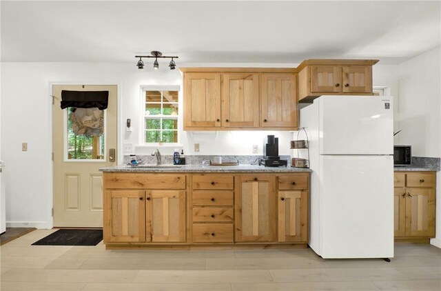 kitchen with white fridge, light stone countertops, light hardwood / wood-style floors, and sink