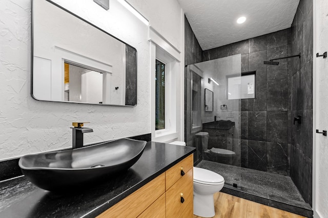 bathroom with hardwood / wood-style floors, vanity, tiled shower, toilet, and a textured ceiling