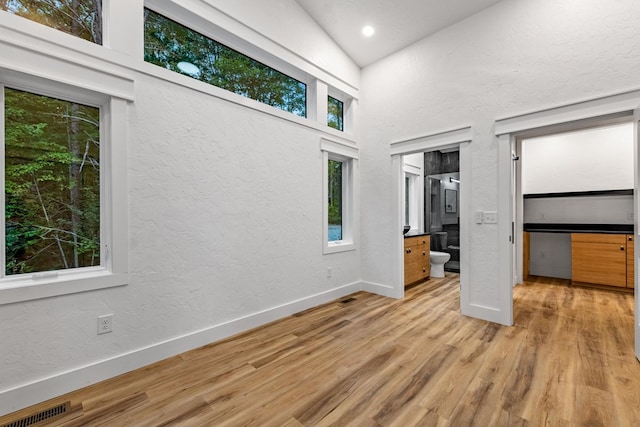 unfurnished bedroom featuring connected bathroom, high vaulted ceiling, and light wood-type flooring