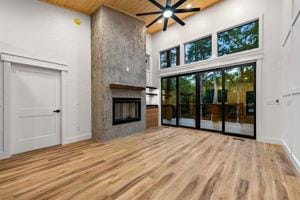 unfurnished living room featuring ceiling fan, a towering ceiling, wood-type flooring, a large fireplace, and wooden ceiling