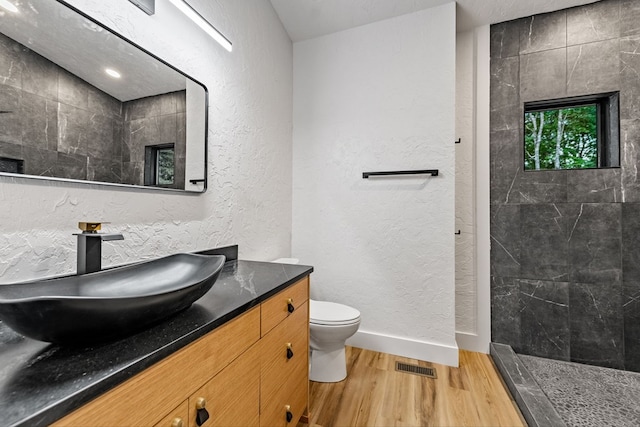 bathroom with vanity, hardwood / wood-style flooring, toilet, and tiled shower