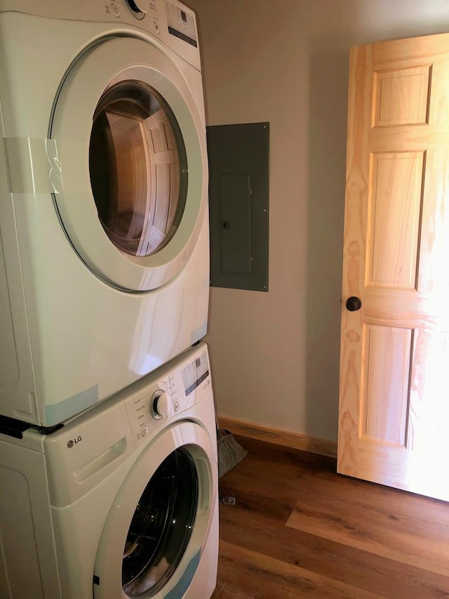 clothes washing area with dark wood-type flooring, stacked washer and dryer, and electric panel