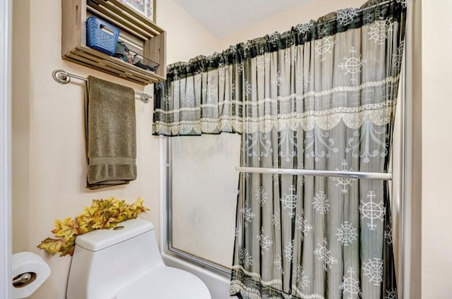 bathroom featuring toilet, shower / bath combination with glass door, and a textured ceiling