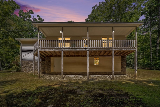 back house at dusk featuring a wooden deck and a yard