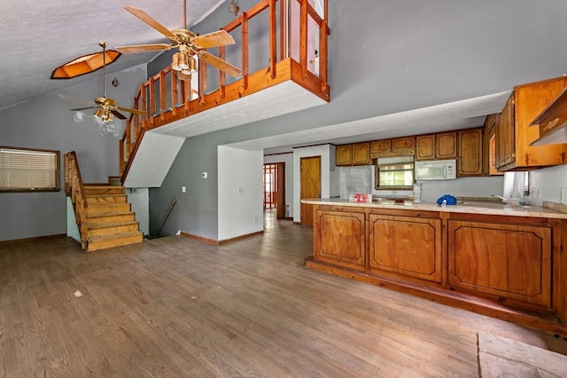 15.20 Piney Acres Rd, Blue Ridge, GA 30513 - kitchen with a ceiling fan, brown cabinetry, white microwave, high vaulted ceiling, and light wood-style flooring