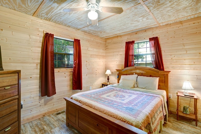 bedroom with light hardwood / wood-style flooring, wooden walls, and ceiling fan