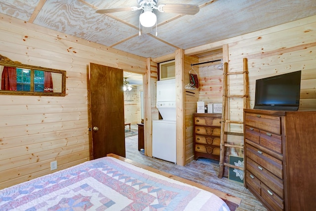 bedroom featuring wood walls, ceiling fan, stacked washer / dryer, and light wood-type flooring