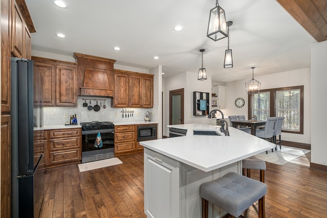 kitchen featuring a sink, light countertops, black appliances, tasteful backsplash, and custom range hood