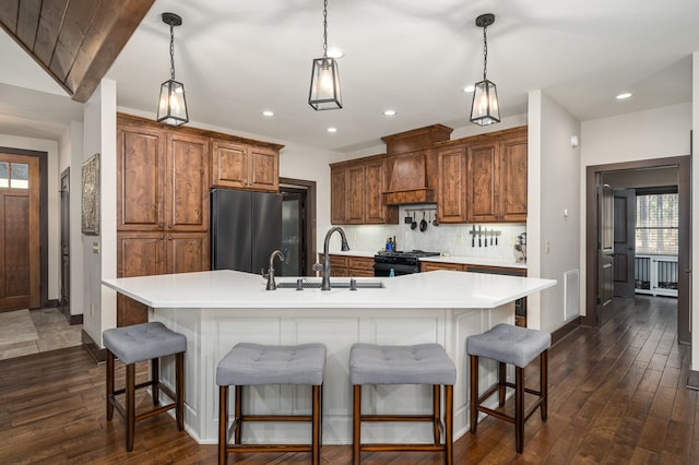 kitchen with a sink, freestanding refrigerator, tasteful backsplash, black gas range oven, and custom range hood