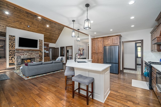 kitchen featuring black gas range oven, freestanding refrigerator, a sink, a stone fireplace, and a kitchen breakfast bar