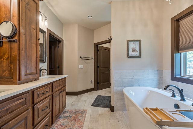 full bathroom featuring double vanity, wood finished floors, a soaking tub, and a sink