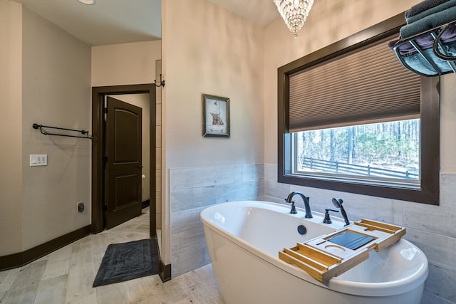 bathroom with wainscoting, tile walls, a freestanding bath, and wood finished floors