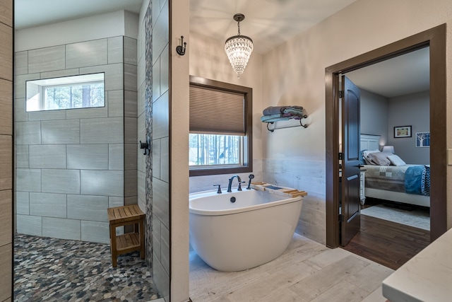 ensuite bathroom featuring a soaking tub, a healthy amount of sunlight, tile walls, and wainscoting