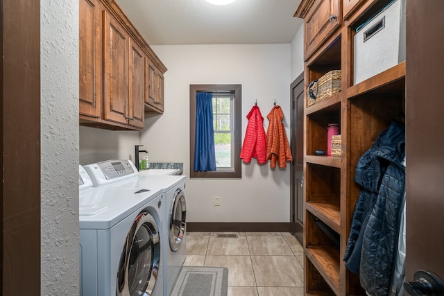 clothes washing area with light tile patterned floors, cabinet space, a textured ceiling, separate washer and dryer, and baseboards