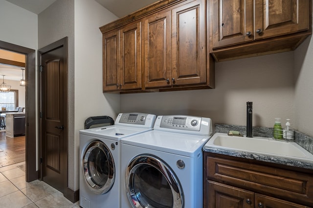 laundry room featuring cabinet space, light tile patterned floors, washer and clothes dryer, and a sink