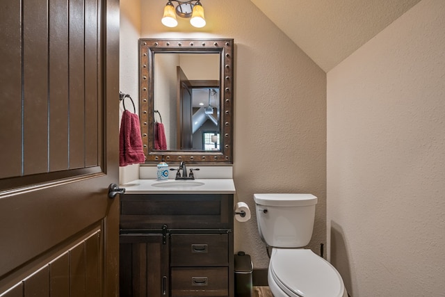 half bathroom featuring toilet, a textured wall, vaulted ceiling, and vanity