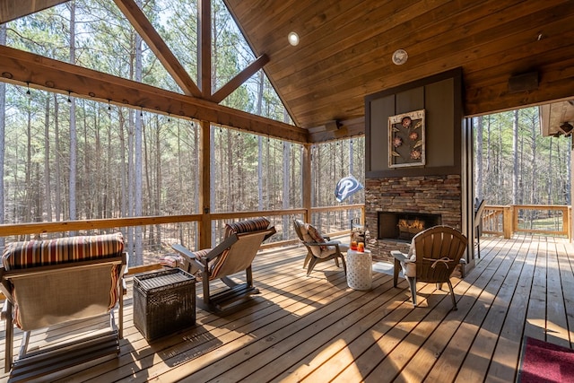 sunroom / solarium featuring lofted ceiling, a fireplace, a wooded view, and a wealth of natural light